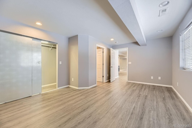 unfurnished bedroom with beamed ceiling, light hardwood / wood-style floors, and a closet