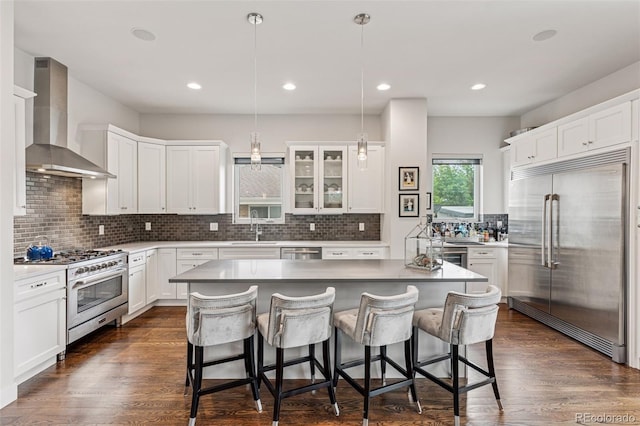 1373 S Garfield St, Denver, CO 80210 - kitchen with high quality appliances, wall chimney range hood, a kitchen breakfast bar, decorative backsplash, and white cabinetry