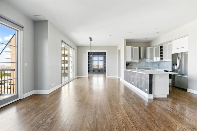 kitchen with tasteful backsplash, light countertops, white cabinets, stainless steel fridge, and wall chimney exhaust hood