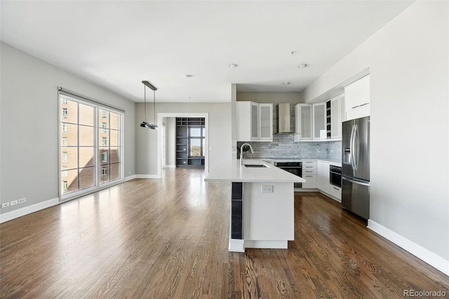 kitchen with a peninsula, a sink, stainless steel refrigerator with ice dispenser, wall oven, and wall chimney range hood