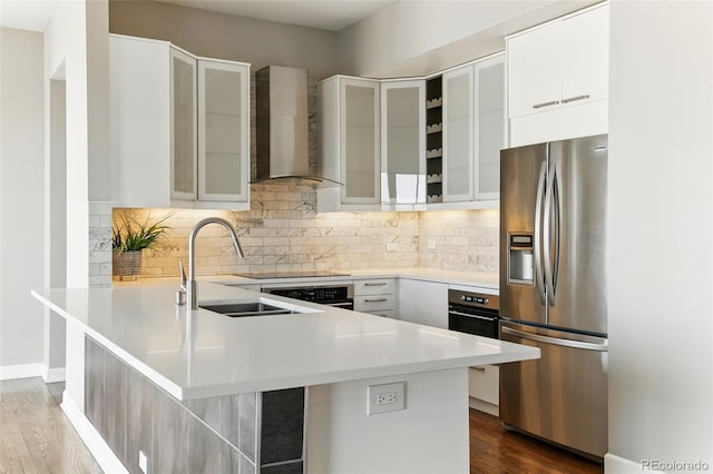 kitchen with a peninsula, stainless steel appliances, modern cabinets, wall chimney exhaust hood, and a sink