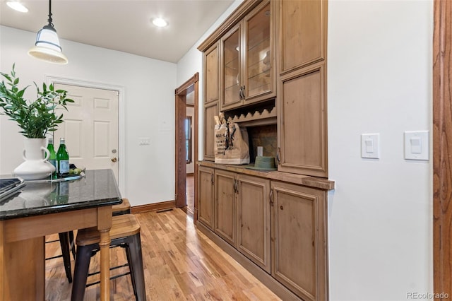 3039 W 22nd Ave, Denver, CO 80211 - kitchen featuring light wood-type flooring, hanging light fixtures, recessed lighting, dark stone counters, and glass insert cabinets