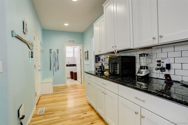 kitchen featuring white cabinetry, decorative backsplash, light wood-type flooring, and dark stone counters