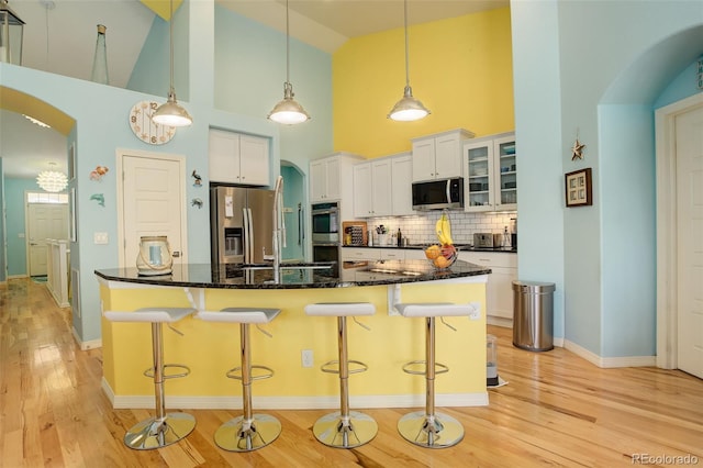 kitchen with appliances with stainless steel finishes, a breakfast bar, white cabinets, and decorative light fixtures