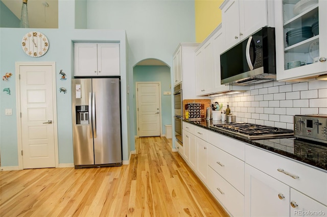 kitchen with dark stone countertops, light wood-type flooring, appliances with stainless steel finishes, decorative backsplash, and white cabinets