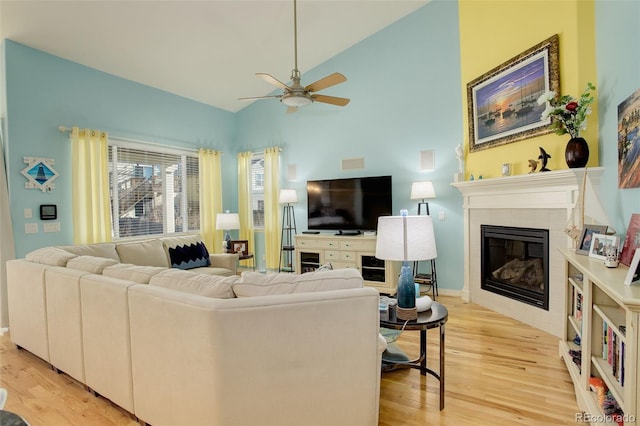 living room with a tiled fireplace, lofted ceiling, ceiling fan, and light hardwood / wood-style flooring