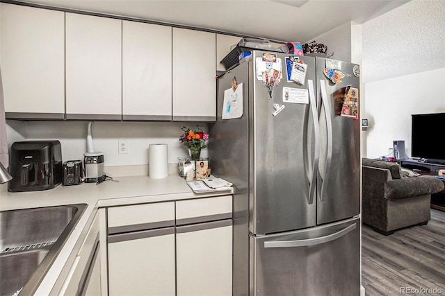 kitchen featuring white cabinetry, a textured ceiling, hardwood / wood-style flooring, and stainless steel refrigerator