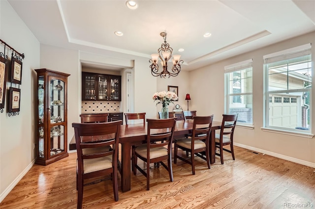 dining space featuring light hardwood / wood-style floors, a raised ceiling, and a notable chandelier