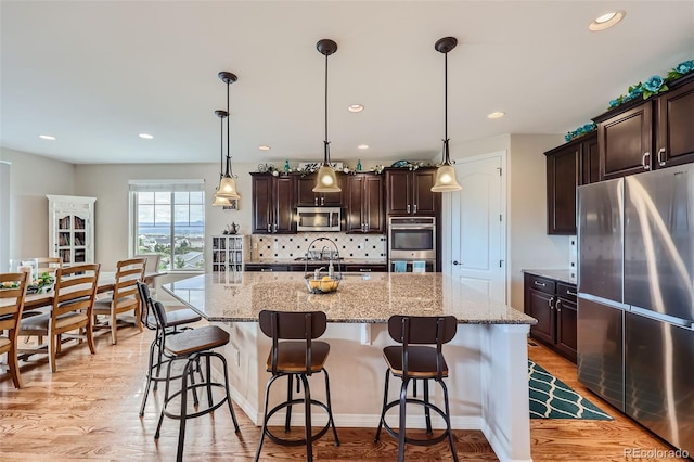 kitchen with appliances with stainless steel finishes, light hardwood / wood-style floors, tasteful backsplash, a center island with sink, and pendant lighting