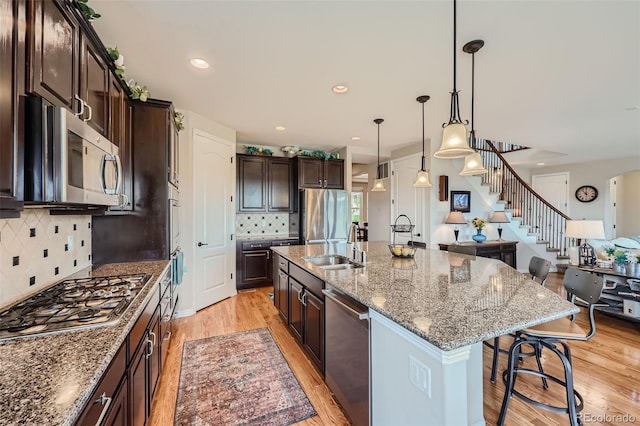 kitchen with stone counters, a breakfast bar, appliances with stainless steel finishes, light wood-style floors, and dark brown cabinets