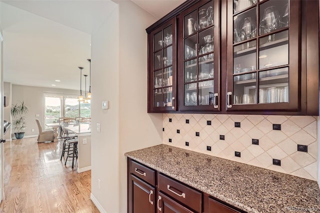 bar featuring dark brown cabinets, tasteful backsplash, light stone counters, light wood-type flooring, and pendant lighting