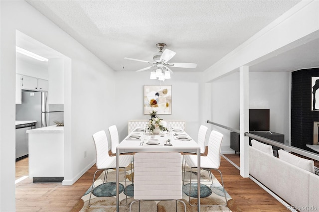 dining area with ceiling fan, a fireplace, light hardwood / wood-style floors, and a textured ceiling