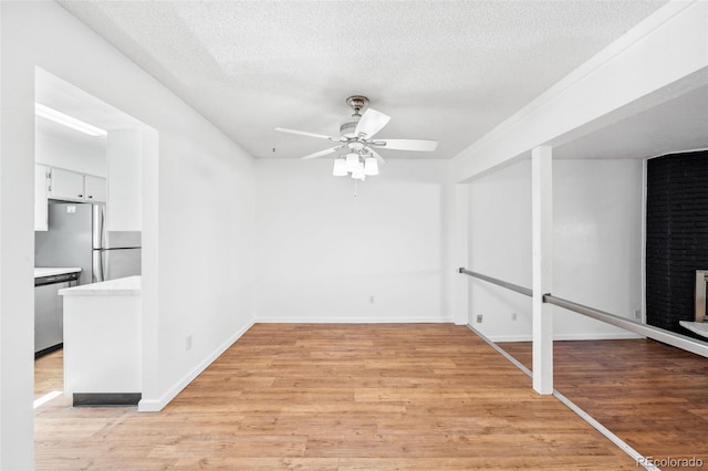 spare room with a fireplace, a textured ceiling, light hardwood / wood-style flooring, and ceiling fan