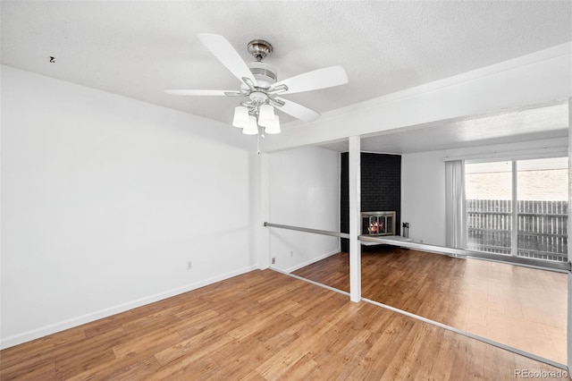 unfurnished bedroom with hardwood / wood-style floors, ceiling fan, a fireplace, and a textured ceiling