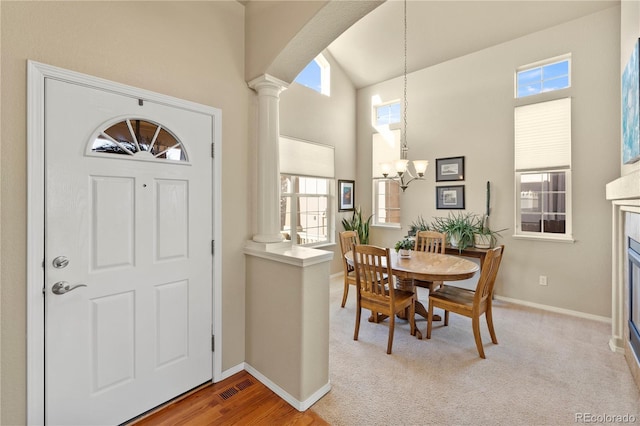 carpeted foyer entrance featuring a chandelier, high vaulted ceiling, and decorative columns