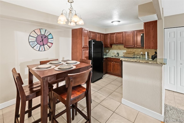 kitchen with freestanding refrigerator, a notable chandelier, light tile patterned floors, hanging light fixtures, and tasteful backsplash