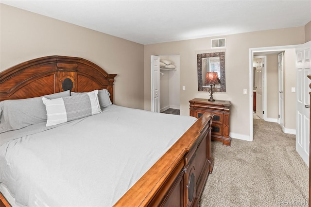 bedroom with a closet, visible vents, light carpet, a walk in closet, and baseboards