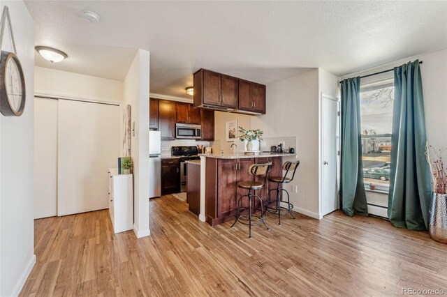 kitchen with a breakfast bar area, a peninsula, light countertops, light wood-style floors, and appliances with stainless steel finishes