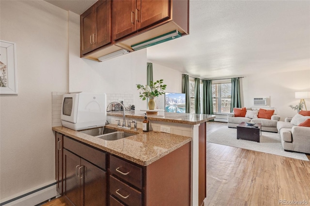 kitchen with a baseboard radiator, light wood-style floors, open floor plan, a sink, and a peninsula