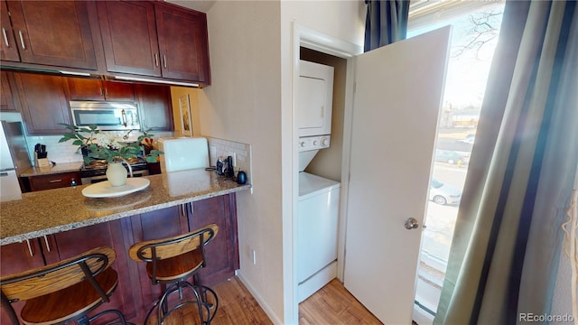 kitchen featuring backsplash, appliances with stainless steel finishes, light stone counters, and stacked washer / drying machine