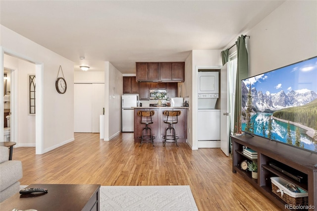 living room with light wood-type flooring, baseboards, and stacked washing maching and dryer
