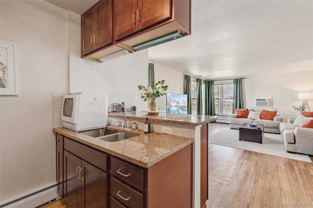 kitchen featuring a baseboard heating unit, open floor plan, light wood-type flooring, a peninsula, and a sink