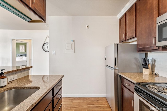 kitchen with light wood-type flooring, stainless steel microwave, light stone counters, and backsplash