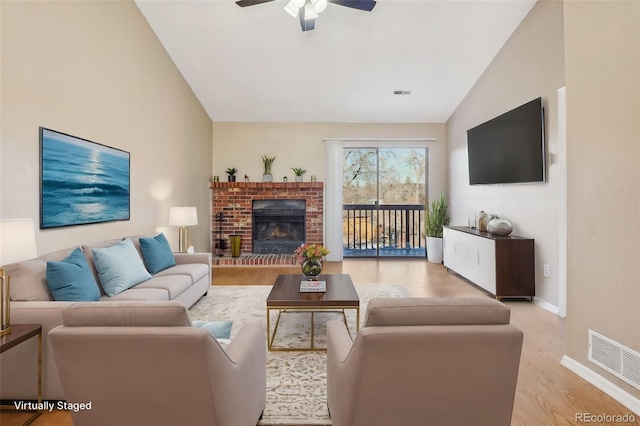 living room featuring ceiling fan, vaulted ceiling, a brick fireplace, and light wood-type flooring