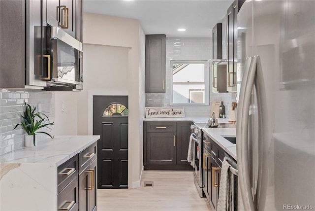 kitchen with stainless steel appliances, decorative backsplash, light stone counters, and light wood-type flooring