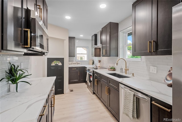 kitchen featuring light wood-type flooring, sink, light stone counters, stainless steel appliances, and backsplash