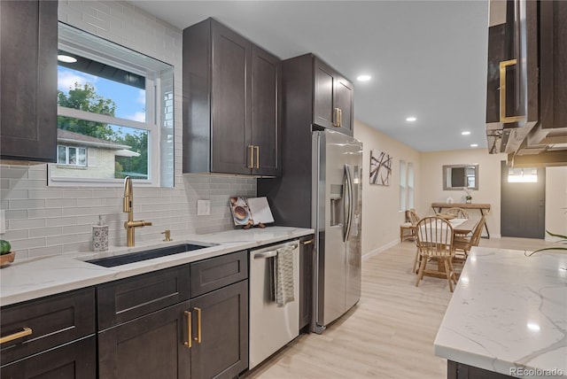 kitchen featuring stainless steel appliances, sink, light wood-type flooring, and light stone counters