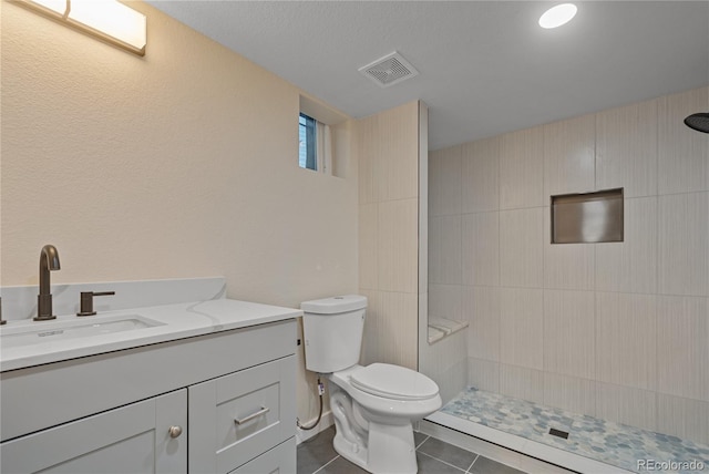 bathroom with tiled shower, tile patterned floors, vanity, and toilet