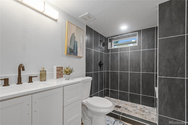 bathroom with vanity, toilet, a textured ceiling, and tiled shower