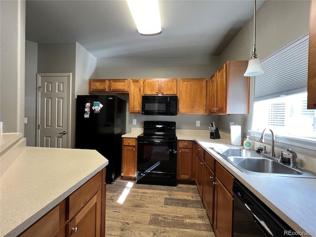 kitchen with black appliances, light wood-type flooring, hanging light fixtures, and sink