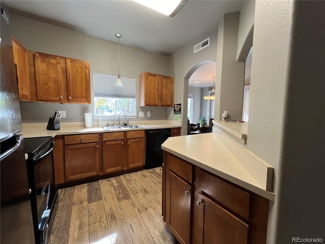 kitchen featuring hanging light fixtures, light hardwood / wood-style floors, black appliances, and sink