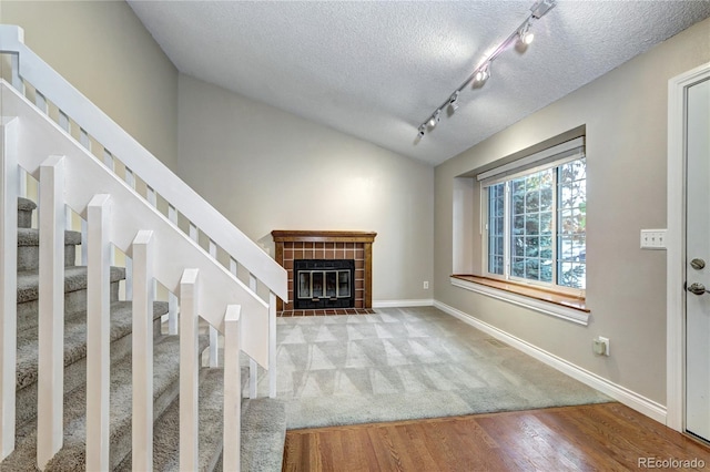 unfurnished living room featuring track lighting, light hardwood / wood-style flooring, lofted ceiling, and a tile fireplace