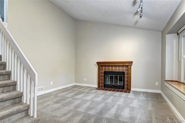 unfurnished living room featuring a tiled fireplace, track lighting, light colored carpet, and a textured ceiling