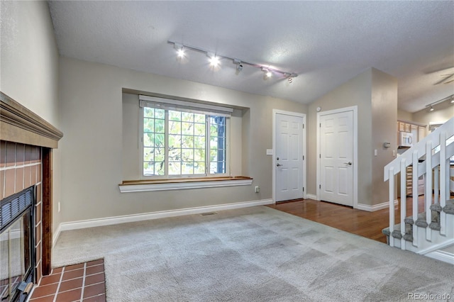 entryway with carpet floors, a textured ceiling, track lighting, a tiled fireplace, and vaulted ceiling