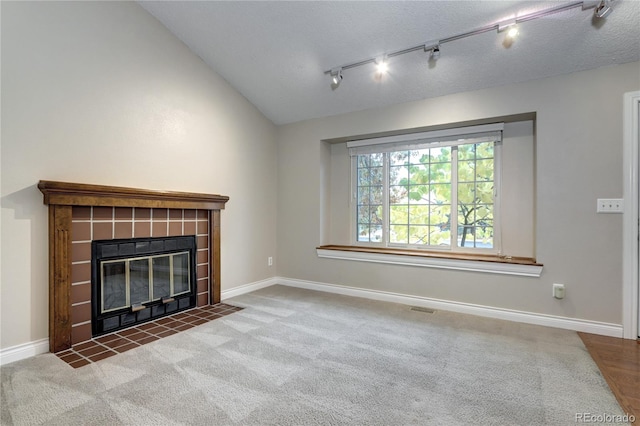 unfurnished living room with dark colored carpet, lofted ceiling, track lighting, a textured ceiling, and a tile fireplace