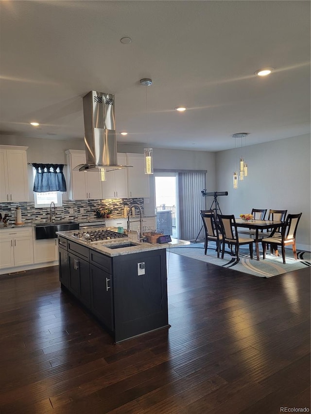 kitchen featuring a kitchen island with sink, a sink, white cabinets, backsplash, and decorative light fixtures