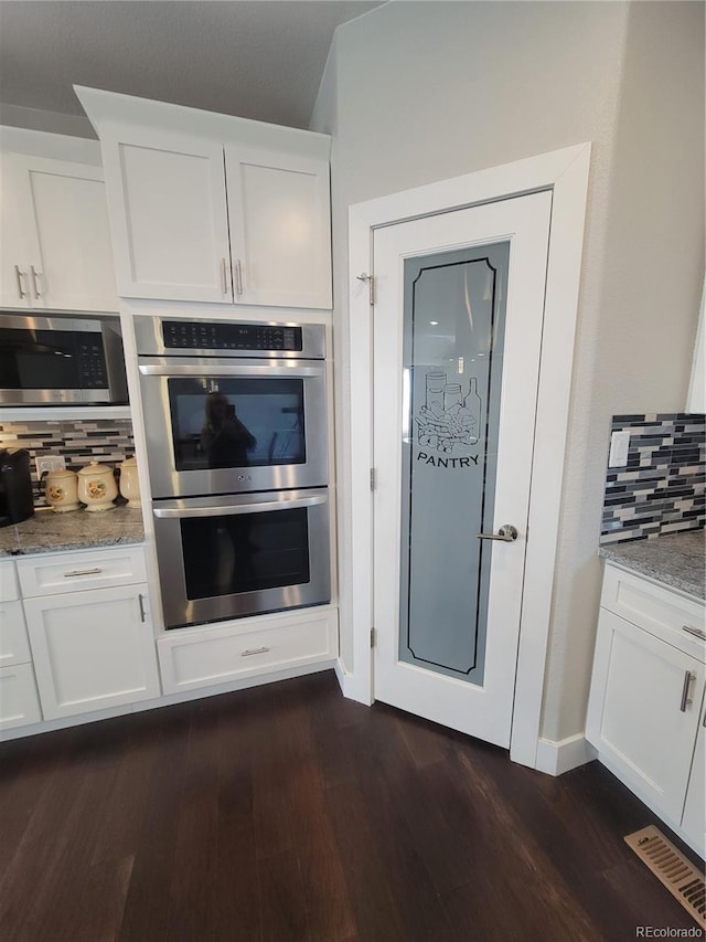 kitchen with visible vents, dark wood finished floors, appliances with stainless steel finishes, light stone counters, and white cabinetry