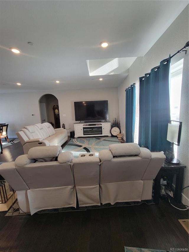 living room featuring arched walkways, dark wood-style flooring, a skylight, and recessed lighting