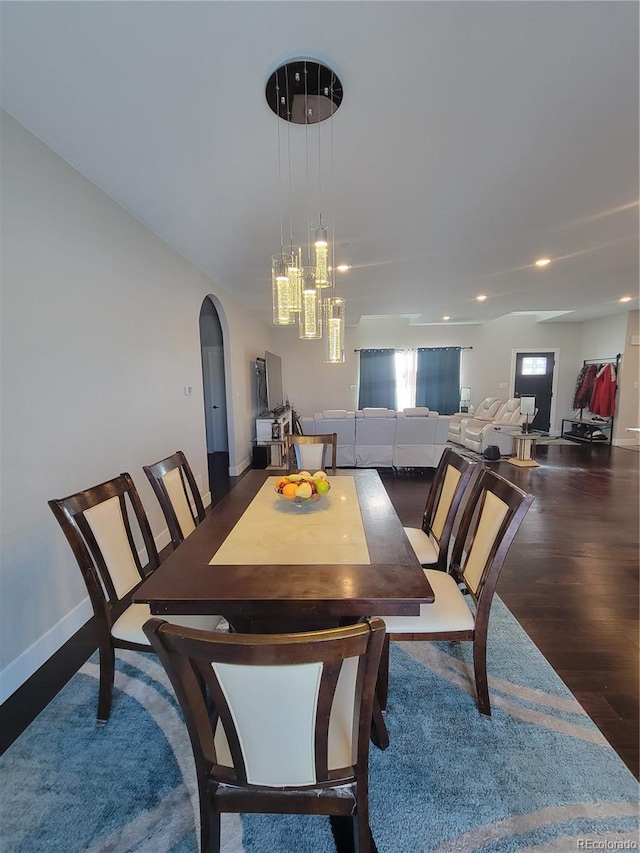 dining area with dark wood-type flooring, arched walkways, and baseboards