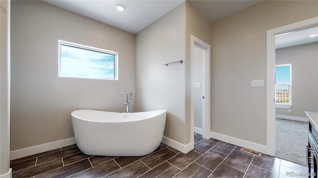 full bath featuring visible vents, baseboards, wood tiled floor, vanity, and a freestanding tub