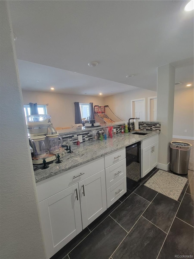 kitchen featuring light stone counters, white cabinets, a sink, a peninsula, and baseboards