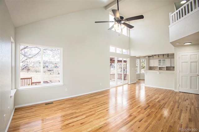 unfurnished living room with beam ceiling, ceiling fan, light hardwood / wood-style flooring, and high vaulted ceiling