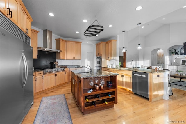 5653 Yank St, Arvada, CO 80002 - kitchen featuring appliances with stainless steel finishes, wall chimney exhaust hood, a sink, light brown cabinets, and a peninsula