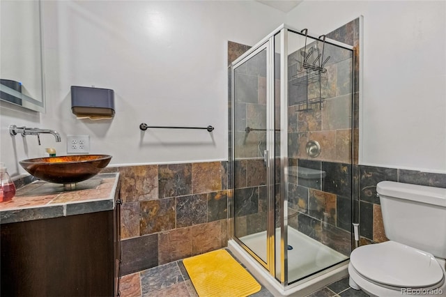 bathroom featuring tile walls, vanity, a shower with shower door, and toilet