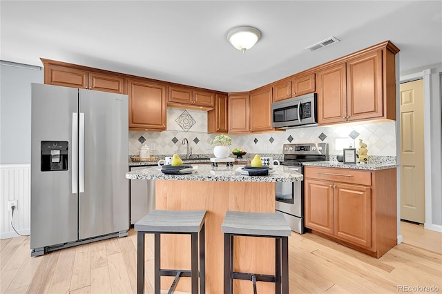 kitchen featuring light stone countertops, appliances with stainless steel finishes, light wood-style flooring, and visible vents