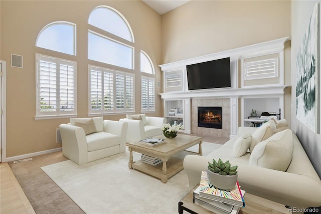 living room with a high ceiling, a tiled fireplace, and hardwood / wood-style flooring